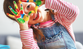 Preschool girl smiling and holding up hands with paint on them.