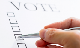 Hand with pen marking on a vote form with American flag in background