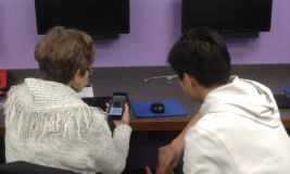 Teen volunteer helping a woman with her cell phone in the Library's Technology Center