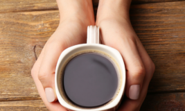 Hands holding a cup of coffee on a wooden table.