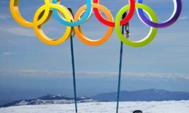Snow-covered mountain with skis and olympic rings on top.
